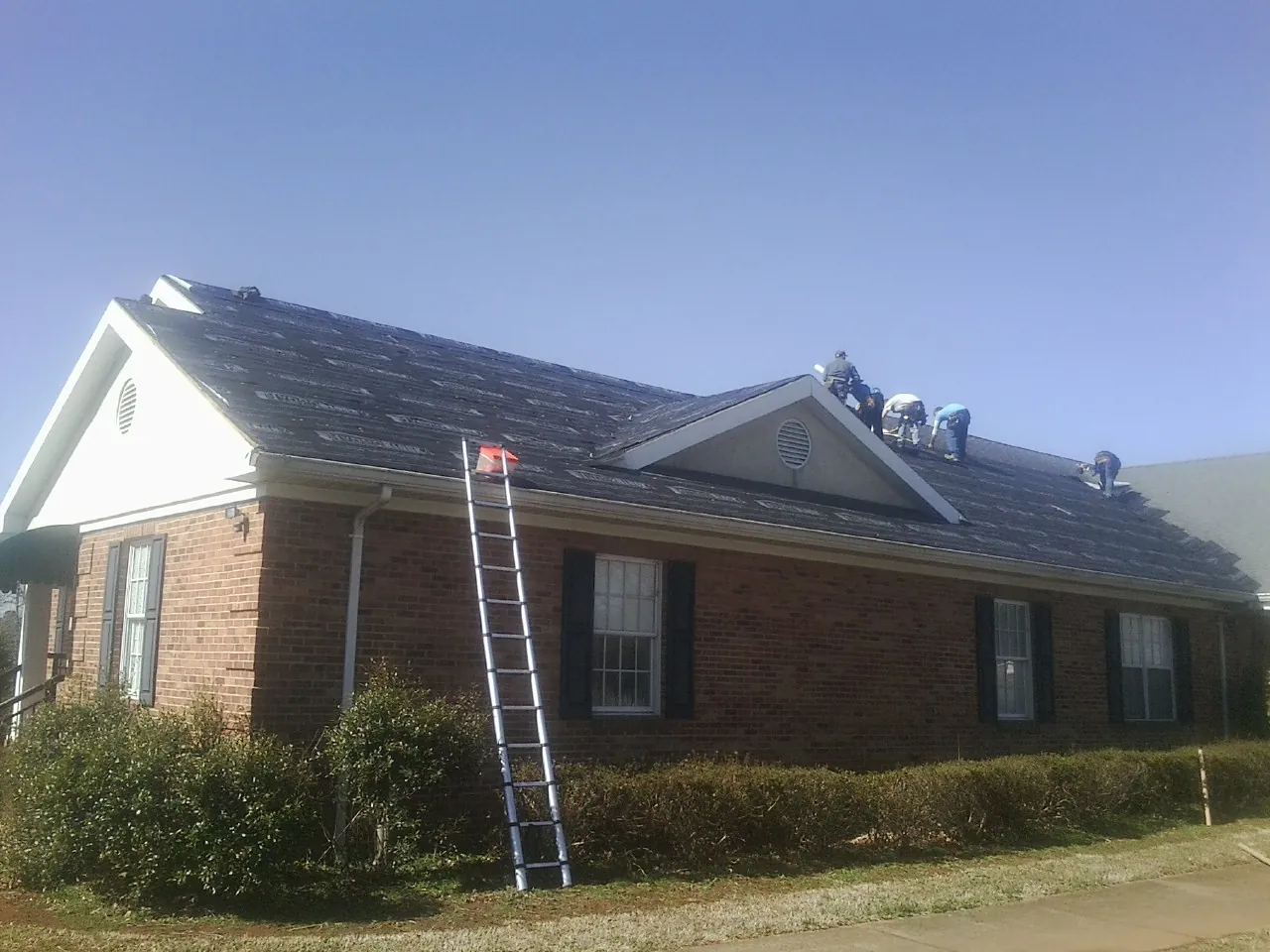 Crew tearing shingles off a brick ranch roof with a ladder set — Metal Roof Repair work by our crew in South Hill