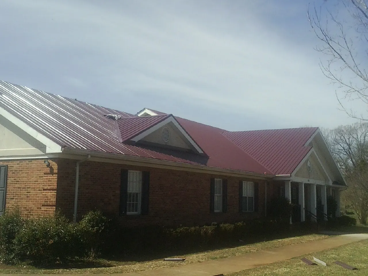 Red metal roof with gabled entries on a long brick building, from a Hail Damage Roof Repair job in South Hill