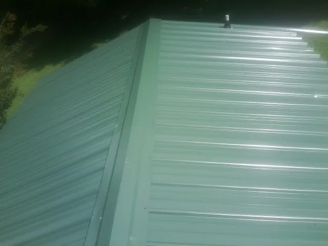New green metal panels meeting at the ridge of a roof — Flat Roof Repair work by our crew in South Hill
