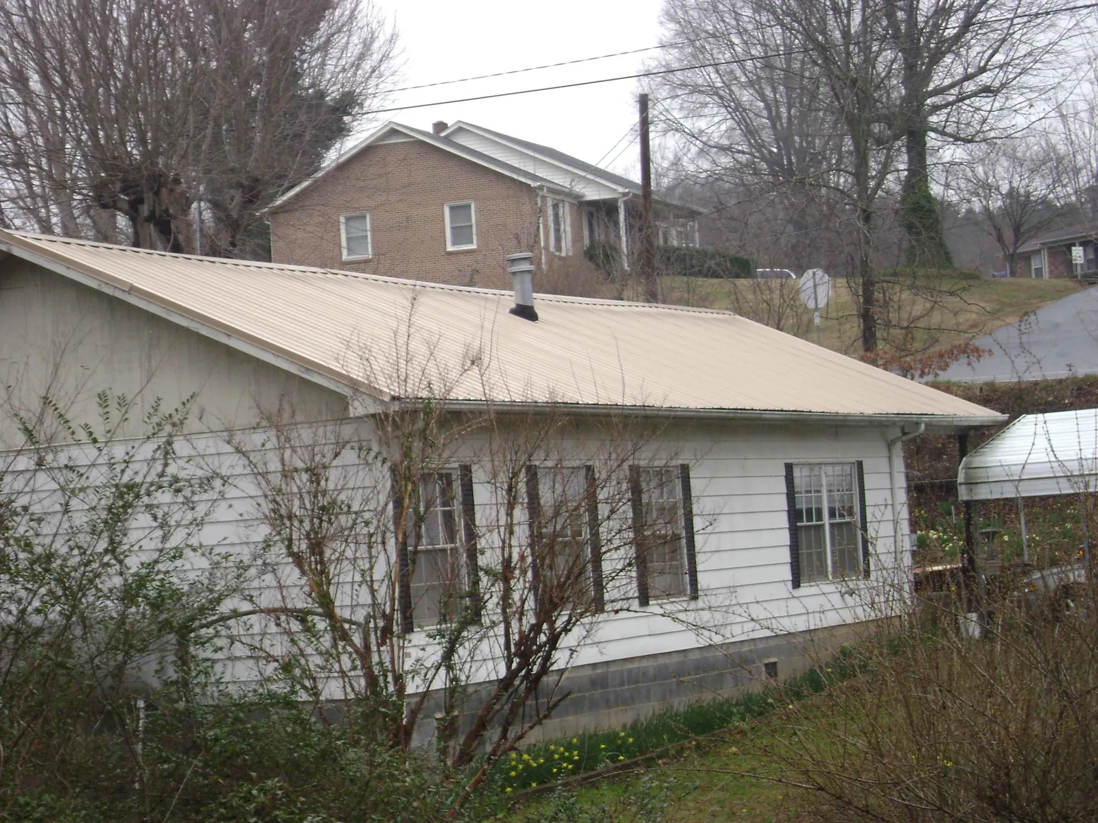 Tan metal roof on a white sided house set into a hillside — Commercial Roofing by Roofing Brothers in South Hill